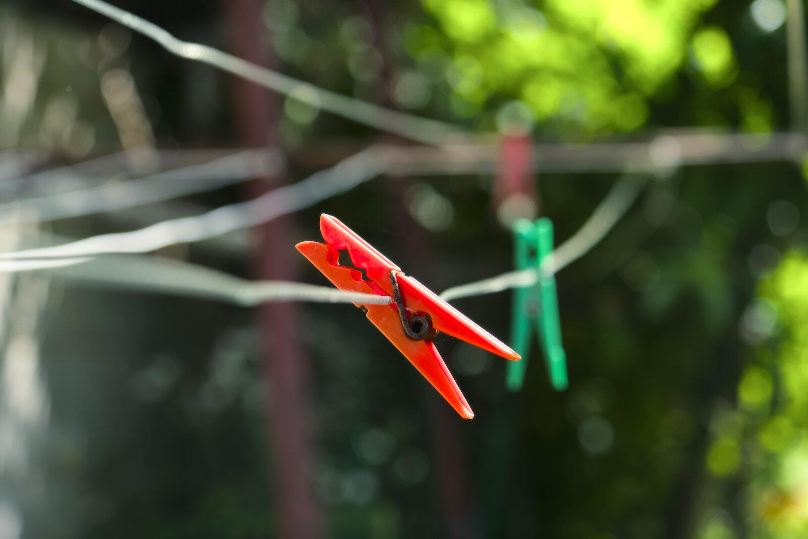 Czerwony spinacz na białym sznurku do bielizny na tle rozmytego zielonego ogrodu, w tle drugi, zielony spinacz.